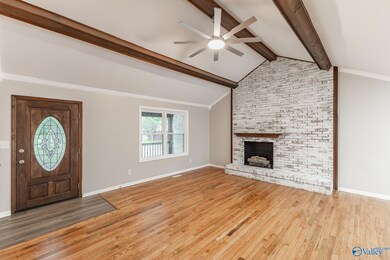 This spacious living area features vaulted ceilings with exposed beams, rich hardwood floors, and a stunning whitewashed brick fireplace—blending warmth and style in one inviting space.