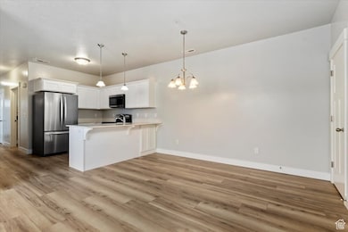 Kitchen with light countertops, appliances with stainless steel finishes, white cabinetry, pendant lighting, and a peninsula