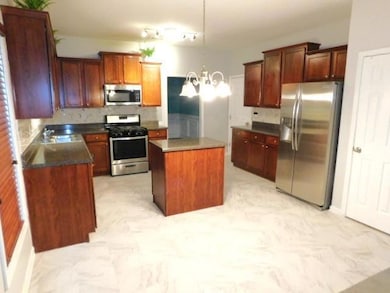 Kitchen with stainless steel appliances, backsplash, a chandelier, a kitchen island, and dark countertops