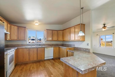Kitchen with a peninsula, pendant lighting, white appliances, brown cabinetry, and ceiling fan