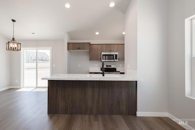 Kitchen with appliances with stainless steel finishes, a peninsula, dark wood-style flooring, decorative light fixtures, and recessed lighting