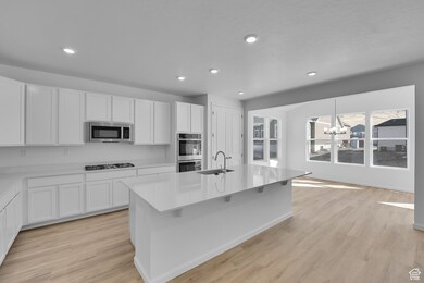 Kitchen with a chandelier, white cabinets, light wood finished floors, a kitchen island with sink, and recessed lighting