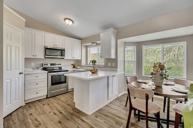 Kitchen with appliances with stainless steel finishes, light countertops, white cabinets, a peninsula, and lofted ceiling