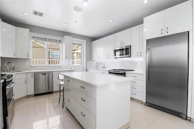 Kitchen with appliances with stainless steel finishes, a kitchen island, white cabinets, light countertops, and recessed lighting