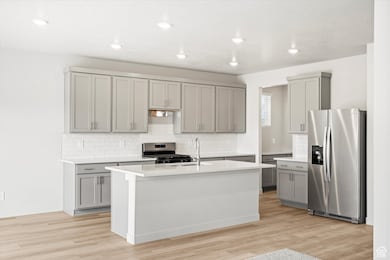 **DISCLAIMER - some exterior and interior options may vary**Kitchen with gray cabinetry, appliances with stainless steel finishes, light wood-type flooring, backsplash, and recessed lighting
