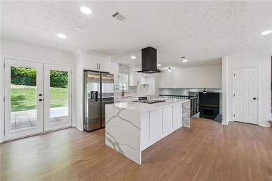 Kitchen with stainless steel refrigerator with ice dispenser, island exhaust hood, light wood finished floors, a center island, and white cabinetry