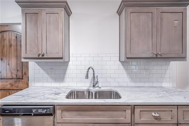 Kitchen featuring dishwashing machine, a sink, tasteful backsplash, and light stone countertops