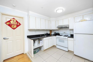 Kitchen featuring white appliances, dark countertops, under cabinet range hood, white cabinetry, and open shelves