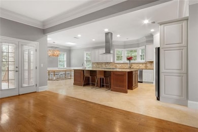 Kitchen featuring ornamental molding, a spacious island, french doors, island exhaust hood, and white cabinets