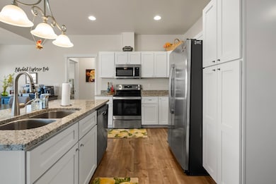 Kitchen with appliances with stainless steel finishes, white cabinetry, decorative light fixtures, light stone counters, and dark wood finished floors