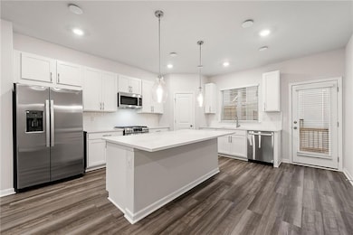 Kitchen featuring white cabinetry, stainless steel appliances, decorative light fixtures, and dark hardwood / wood-style flooring
