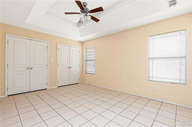 Unfurnished bedroom featuring visible vents, multiple closets, a tray ceiling, light tile patterned floors, and a ceiling fan