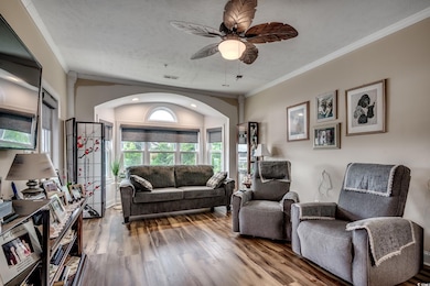 Living area featuring ornamental molding, wood finished floors, a ceiling fan, arched walkways, and a textured ceiling
