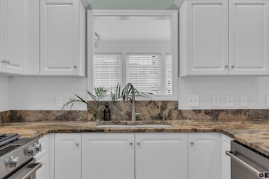 Kitchen with a sink, white cabinetry, dark stone c