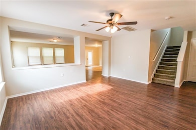 Unfurnished living room featuring stairway, dark wood-style flooring, and a ceiling fan