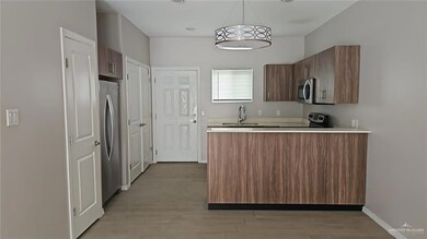 Kitchen featuring a peninsula, light countertops, brown cabinetry, decorative light fixtures, and appliances with stainless steel finishes