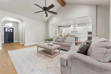 Living area featuring arched walkways, a ceiling fan, high vaulted ceiling, beamed ceiling, and light wood finished floors