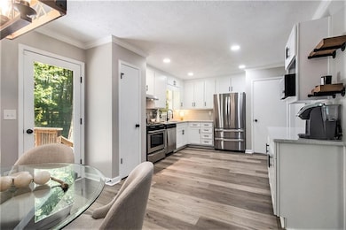 Kitchen with appliances with stainless steel finishes, crown molding, light wood finished floors, light countertops, and recessed lighting