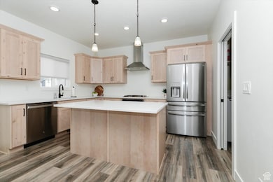 Kitchen with light countertops, wall chimney exhaust hood, stainless steel appliances, a center island, and light brown cabinetry