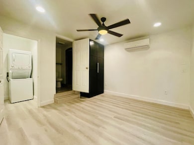 Unfurnished bedroom with light wood finished floors, arched walkways, estacked washer and dryer, recessed lighting, and ceiling fan