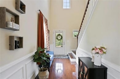 Entryway with stairs, a high ceiling, dark wood-type flooring, and a wainscoted wall