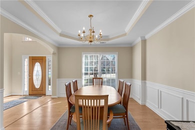 Dining space with a chandelier, a tray ceiling, arched walkways, light wood-style flooring, and ornamental molding