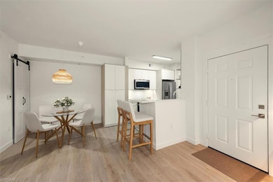 Kitchen with appliances with stainless steel finishes, a kitchen bar, white cabinets, light wood-style floors, and a barn door