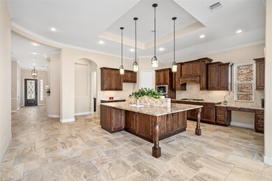 Your chef's kitchen has rich wooden cabinetry, a central island, granite countertops, modern pendant lighting,  high ceilings, tiled flooring and opens to a welcoming entryway.