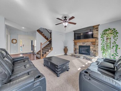 Living room with hardwood / wood-style flooring, a stone fireplace, and ceiling fan