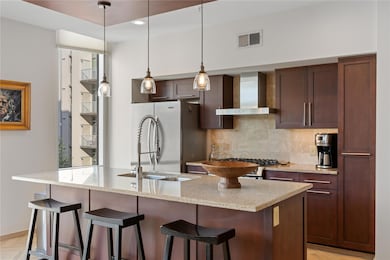 Kitchen featuring decorative light fixtures, light stone counters, wall chimney exhaust hood, and a breakfast bar