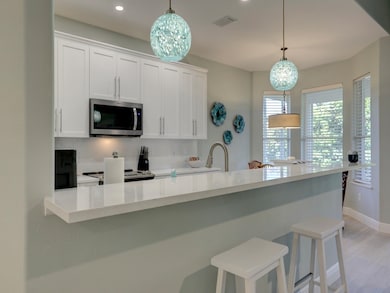 Kitchen with white cabinetry, stainless steel appliances, light stone counters, decorative light fixtures, and a kitchen bar