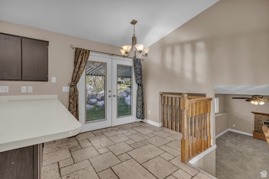 Unfurnished dining area with french doors, lofted ceiling, a chandelier, light carpet, and stone tile floors