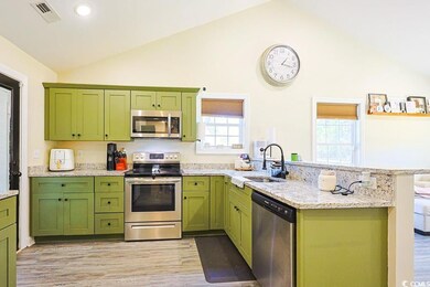 Kitchen featuring green cabinetry, appliances with stainless steel finishes, a peninsula, vaulted ceiling, and light stone counters