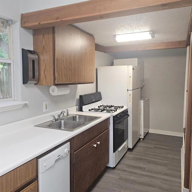 1015 Kitchen featuring range with gas cooktop, white dishwasher, a sink, light countertops, and dark wood finished floors