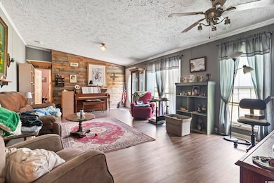 Living room featuring wooden walls, vaulted ceiling, ceiling fan, a textured ceiling, and wood finished floors