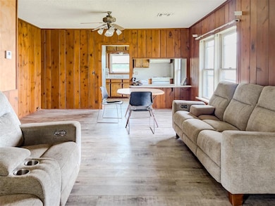 Living area with plenty of natural light, wooden walls, ceiling fan, and light wood finished floors