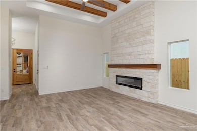 Unfurnished living room with a stone fireplace, light wood-style flooring, beamed ceiling, and a towering ceiling