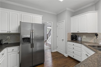 Kitchen featuring decorative backsplash, stainless steel fridge with ice dispenser, white cabinetry, dark stone counters, and ornamental molding