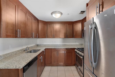 Kitchen with appliances with stainless steel finishes, light tile patterned floors, and brown cabinetry
