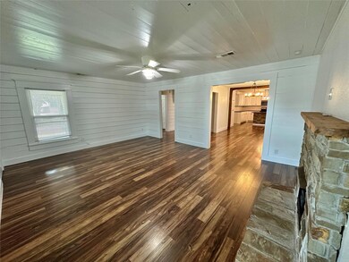 Unfurnished living room featuring dark hardwood / wood-style floors, wooden walls, ceiling fan with notable chandelier, and a stone fireplace