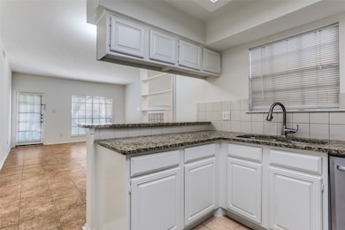 Kitchen featuring white cabinets, decorative backsplash, light tile patterned floors, dark stone countertops, and stainless steel dishwasher