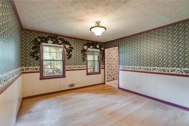 Unfurnished room featuring ornamental molding, wood-type flooring, a textured ceiling, wallpapered walls, and wainscoting