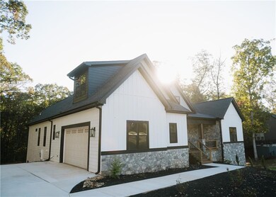View of side of home featuring stone siding, a garage, a porch, concrete driveway, and roof with shingles