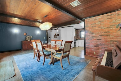 Dining room with brick wall, wood finished floors, a wooden ceiling with exposed beams, and a chandelier