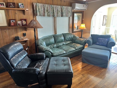 Living room featuring arched walkways, a wall mounted air conditioner, wood finished floors, and wooden walls