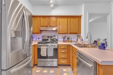 Kitchen with appliances with stainless steel finishes, under cabinet range hood, light countertops, brown cabinetry, and a textured ceiling