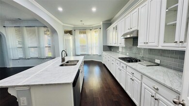 Kitchen featuring white cabinets, a sink, appliances with stainless steel finishes, under cabinet range hood, and crown molding