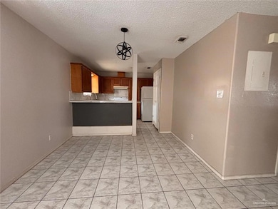 Kitchen featuring tasteful backsplash, hanging light fixtures, white fridge, electric panel, and kitchen peninsula