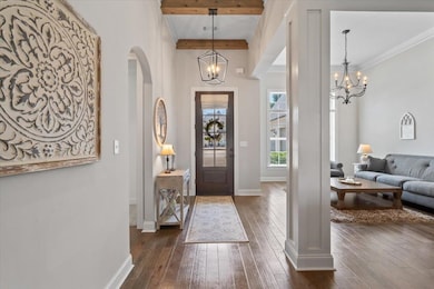 Foyer with a chandelier, dark wood-type flooring, arched walkways, and ornamental molding