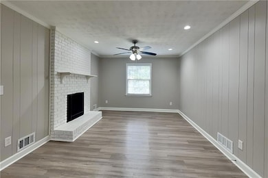 Unfurnished living room featuring ornamental molding, ceiling fan, wood finished floors, a brick fireplace, and a textured ceiling